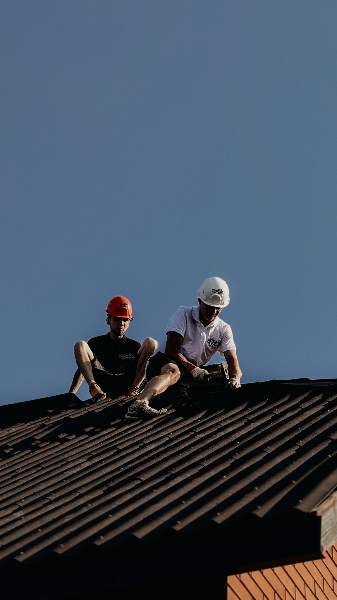 Two construction workers in helmets repairing a roof on a clear day, enhancing safety and teamwork.